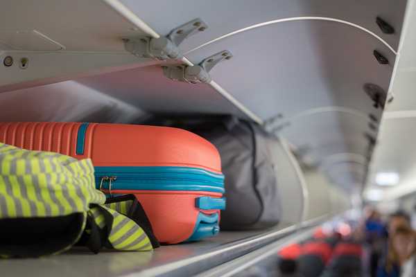 A person putting their cabin bag in an overhead locker on a plane.